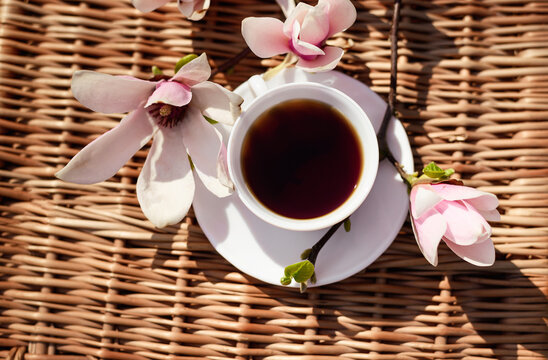 white cup with coffee on the background of a wicker basket with magnolia flowers. Spring still life composition. good morning concept. cup with tea on vmd terrace from above.