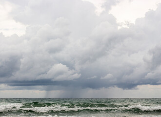 A summer day with waves and a blue sky. A dark sea shoreline with storm clouds in the sky.