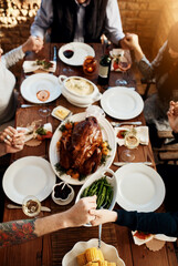 Food, table and people praying and holding hands while eating together for holiday celebration. Above group of family or friends pray for thanksgiving lunch, chicken or turkey and wine drinks