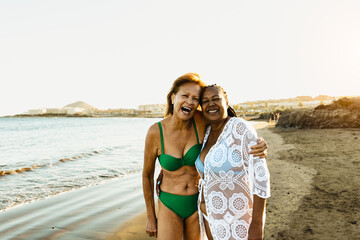 Happy senior multiracial women having fun on the beach during summer holidays - Diverse elderly...