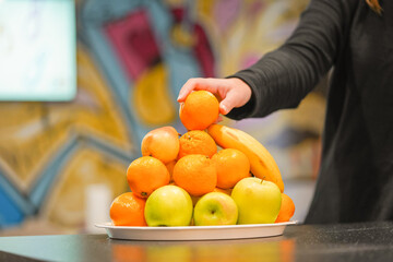 Hand of a girl taking the fruit off the plate in a modern designed room office space during fruit day perks and benefits for the employees