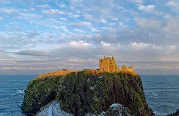 Dunnottar Castle perched high on the Conglomerate Cliffs lit up by the setting evening light of a...