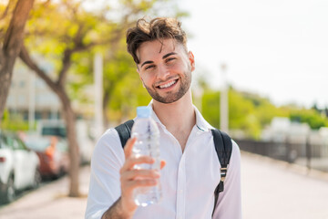 Young handsome man with a bottle of water at outdoors with happy expression