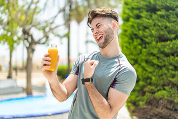 Young handsome sport man holding an orange juice at outdoors celebrating a victory