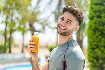 Young handsome sport man holding an orange juice at outdoors smiling a lot