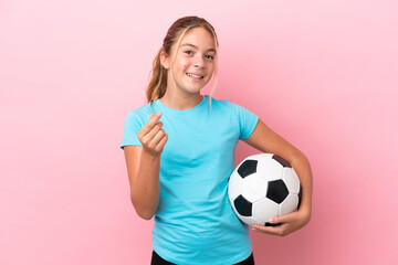 Little football player girl isolated on pink background making money gesture