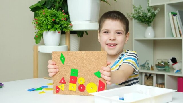 A preschooler shows a picture of a mosaic - a board with wooden parts nailed with a hammer. Hammer games for baby