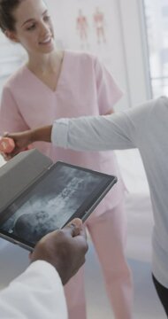 Vertical video of diverse male doctor with tablet, female physio and senior patient, slow motion