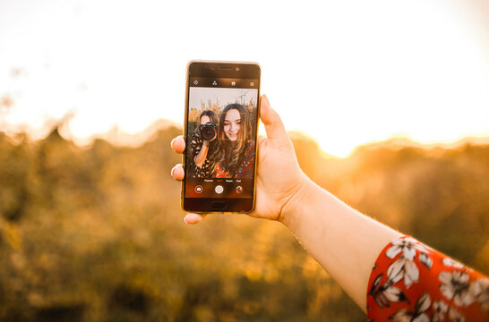 two girls are photographed taking a selfie on the phone in nature at sunset