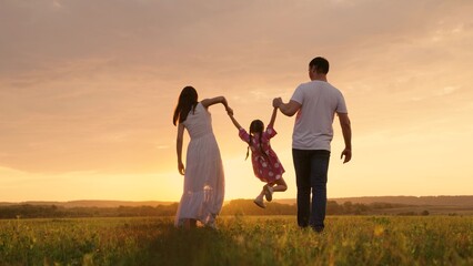 Parents, daughter run at sunset, kid holds hands of his parents and jumps. Active family playing in...