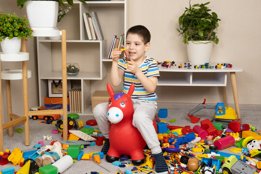 A little boy is jumping on an inflatable rubber donkey among the mess in the children's room. Bouncing toy for kids.