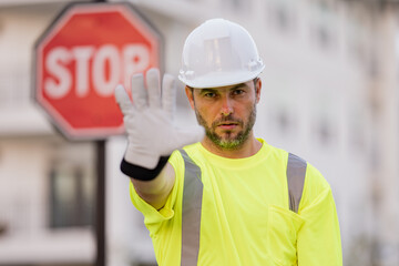 Serious engineer with stop road sign. Builder with stop gesture, no hand, dangerous on building concept. Man in helmet showing stop road sign.
