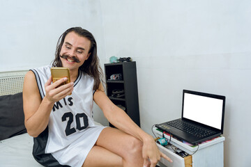 young person of non-binary gender very happy watching his phone smiling, in his room.