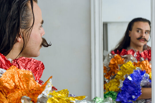 non-binary young person dressed as a drag queen looking in the mirror thinking.
