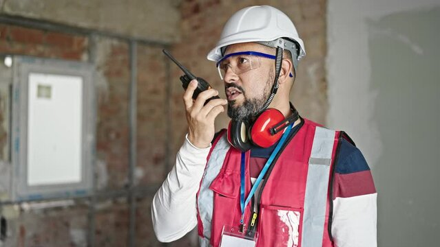 Young latin man builder talking on walkie-talkie at construction site