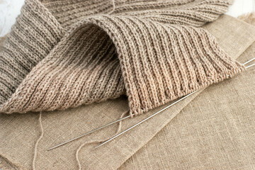 Yarn for knitting on a wooden table. Knitted scarf and balls of yarn close up. Knitting is a kind of needlework and a hobby.