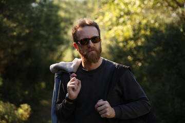 Trekking lover, adventurer, bearded Caucasian man with sunglasses posing in front of a blurry background with soft natural light