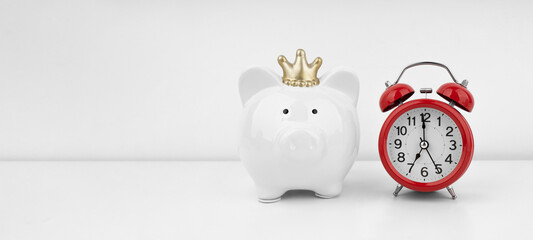 Red alarm clock with piggy bank against a white wall. Financial concept.