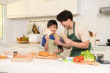 Obraz na płótnie Canvas Happy Young Asian father and son cooking in kitchen at home