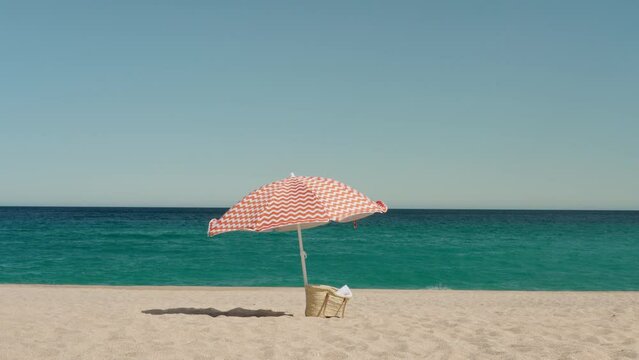 Male tourist walks along the sandy beach, against the backdrop of the sea and clear blue sky. Vibrant red parasol swinging in the wind and flies away. Gone with the wind concept
