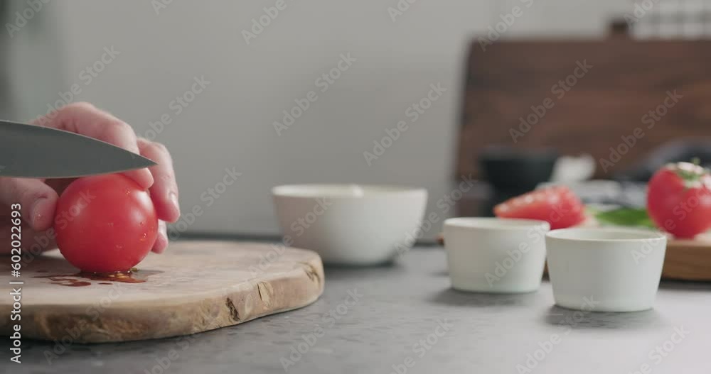 Wall mural Slow motion dolly shot of man slicing tomato on olive wood board