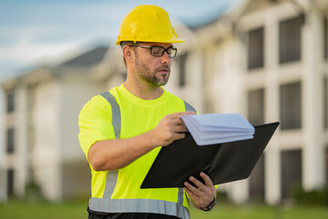 Builder on site construction. Man worker in hard hat. Engineer with clipboard, building inspection. Construction worker in helmet at construction new home building.