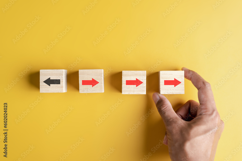 Aufkleber Hand holding woodblock Red arrow and different direction facing opposite direction with black arrow for business disruption and technology transformation and different thinking idea concept.