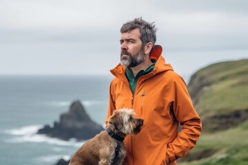 Man with a dog in a raincoat on the wild coast of Iceland
