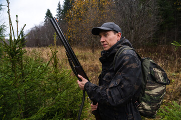 Hunter with a gun and a backpack in the forest.