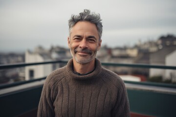 Fototapeta premium Portrait of a handsome middle-aged man with gray hair, wearing a woolen sweater, standing on the roof of a building.