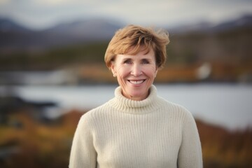 Fototapeta premium Portrait of smiling senior woman standing in front of lake during autumn