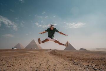 young man with a turban jumps in the desert with the pyramids in the background. Cairo. Egypt	
