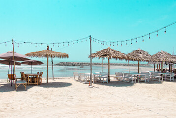 Wooden seaside parasols (Straw Umbrellas) and seats with table on the sand beach landscape in clear blue sky for vacation concept in summer holiday