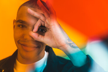 young man making a circle with his fingers near his eye, colorful lense, medium closeup. High quality photo