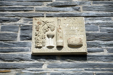Steintafel mit Relief, Weinglas, Weinflasche und Inschrift in Naturfarben auf Mauerwerk aus...