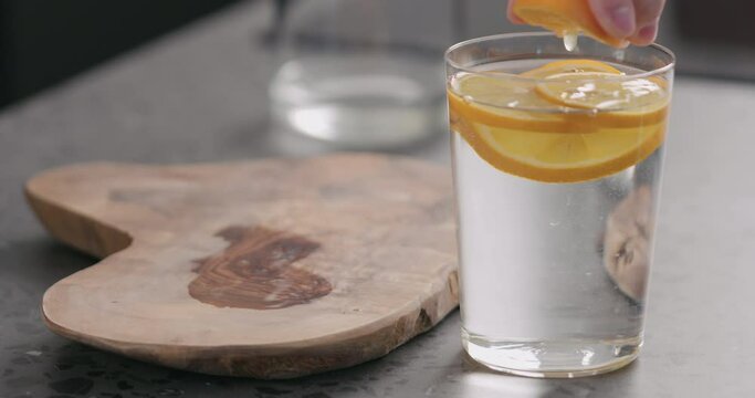 Slow motion man squeeze orange lemon into water in glass