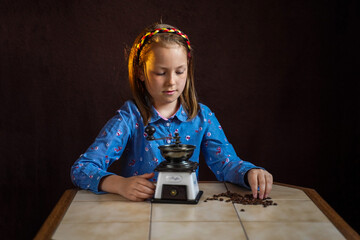 Portrait of a girl in rural clothes and a retro coffee grinder in her hands on a dark background. Medieval little girl.