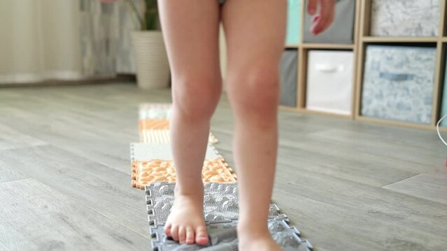 The legs of a small child on orthopedic mats for forming the correct arch of the foot. Massage puzzle mat.