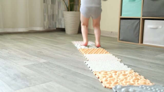 A child jumps barefoot on massage mats. Exercises for legs on the carpet. Orthopedic massage mats for the development of children.