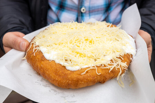 Langos held in hands, Sold in the street, traditional in Eastern Europe, deep-fried dough, Street food served with various toppings, 
