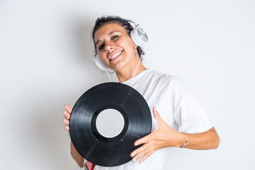 Attractive Latina in white T-shirt, listening to music with headphones from her cell phone, with neutral background, playing with a vinyl record