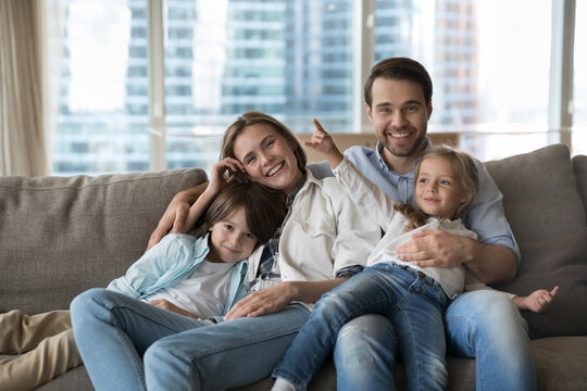 Happy young mother, father and two cheerful children resting together on sofa, enjoying family leisure, warm relationships, childhood, parenthood. Group home portrait