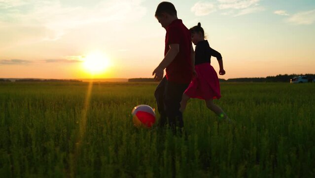 Childrens outdoor play, child, boy, girl playing with ball in park on green grass. Happy children run, kicks ball. Childrens team plays football in meadow. Child, boy, girl playing ball in nature, sun