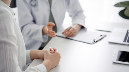 Doctor and patient discussing current health examination while sitting at the desk in clinic office, closeup. Medicine concept