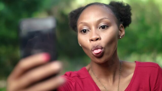 Selfie, tongue or happy black woman in park with nature, smile and happiness. Funny girl, goofy or crazy face female on smartphone for outdoor photo, profile picture update or social media content