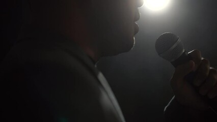 Close up shots microphone speaker man talking on stage with spotlight strike through the darkness at corporate business event. Public speaker giving talk at conference hall. Stand up comedian.