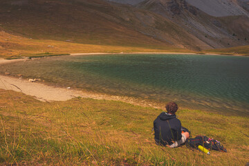 A male hiker sitting next to a mountain lake, Lac de Soulier (Hautes-Alpes)