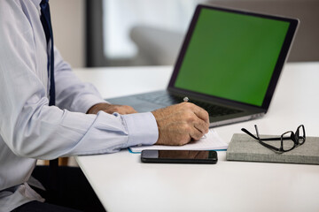 Close up of businessman working and taking notes in his modern office. Directorr CEO using laptop with green screen and signing documents.