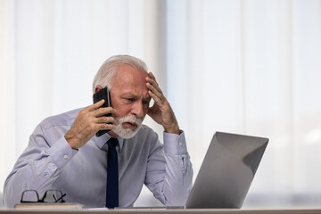 Shocked senior businessman talking on smartphone and using laptop, hearing bad news, unexpected debt or bankruptcy, financial problems. Frustrated upset CEO making phone call - 602079603