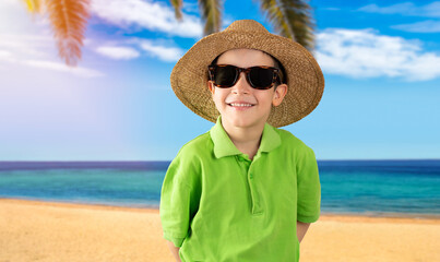 Kid on vacation wearing green t-shirt hat sunglasses at beach happy face smiling and looking at the camera. Positive person